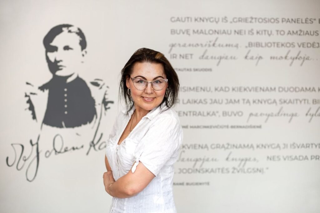 Moteris šypsosi kitos moters portreto ant bibliotekos sienos fone