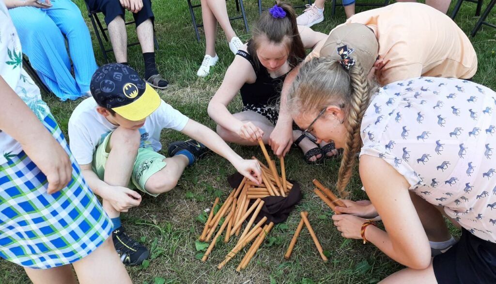 Ant pievos tupi keli berniukai ir mergaitės ir ima edukacijos pagaliukus iš maišiuko