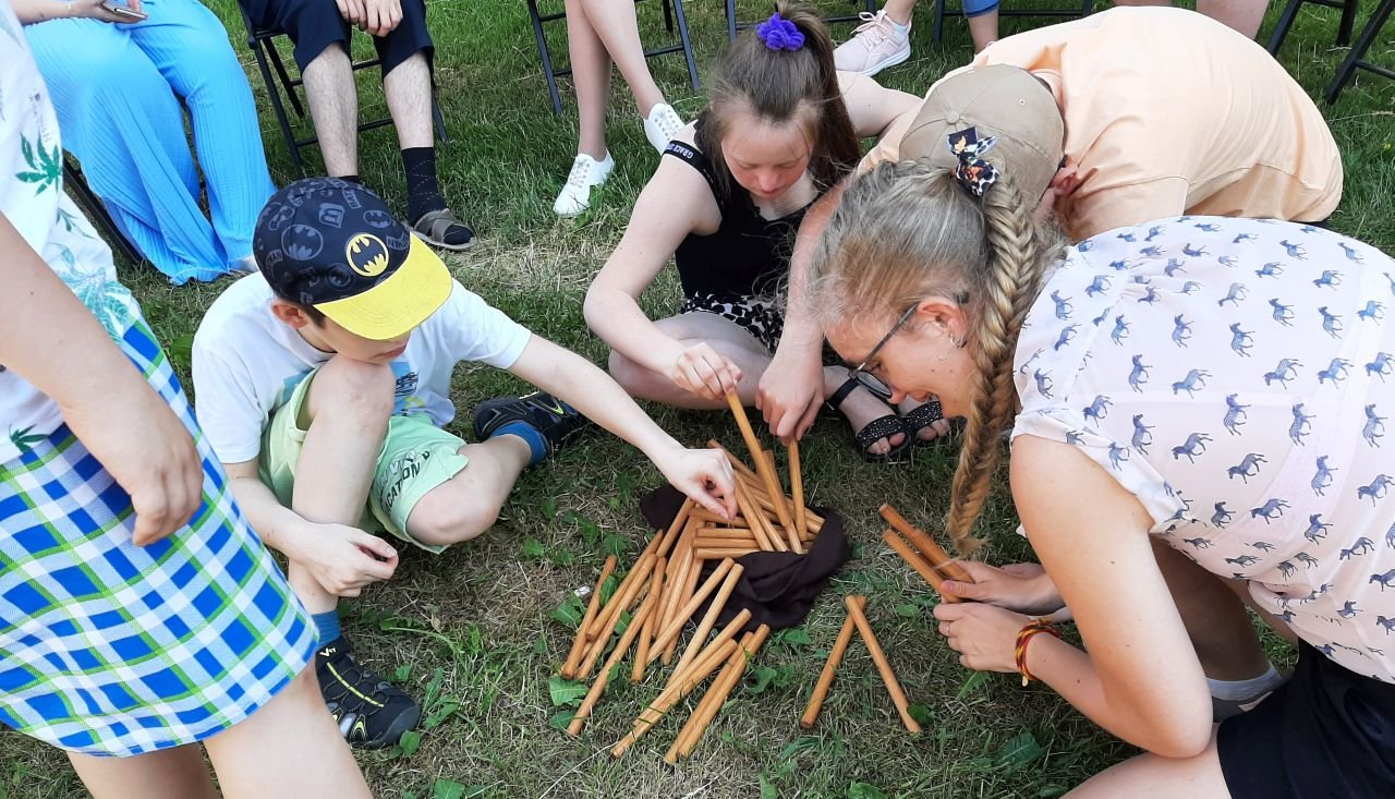 Ant pievos tupi keli berniukai ir mergaitės ir ima edukacijos pagaliukus iš maišiuko
