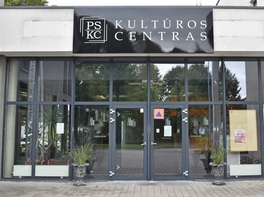 Virš įėjimo pakabintas iškaba "Kultūros centras". Stiklinis fasadas ir durys su tamsiais rėmais.