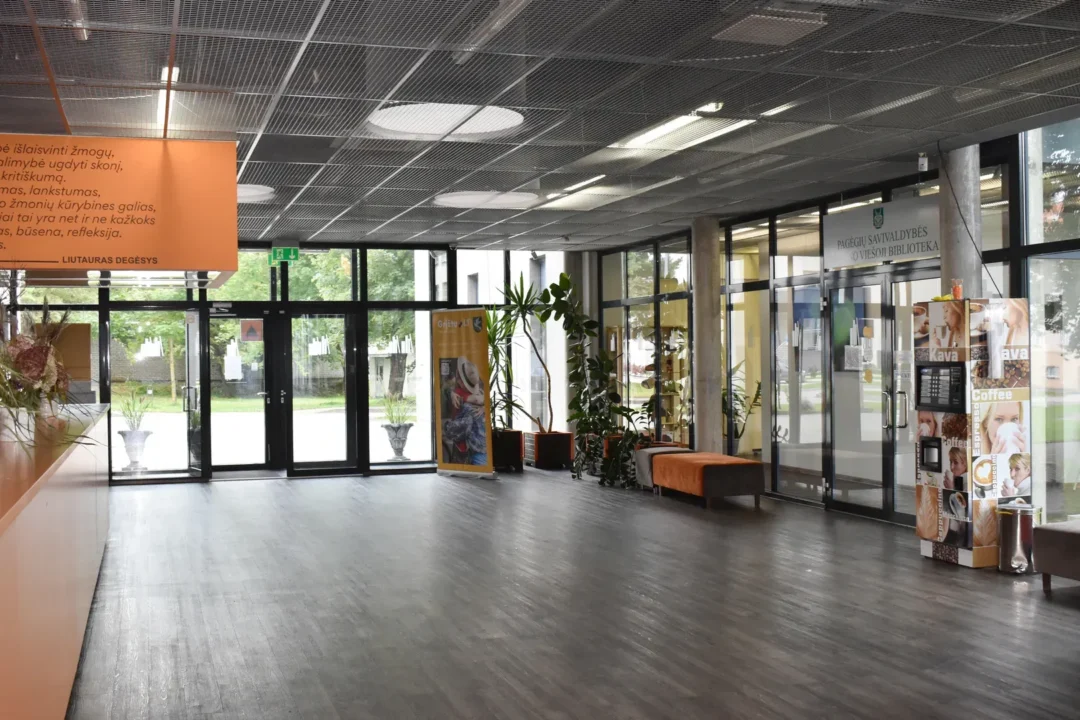 Erdvi foje, kurioje gėlės baldai, kavos pardavimo aparatas prie durų į biblioteką.
